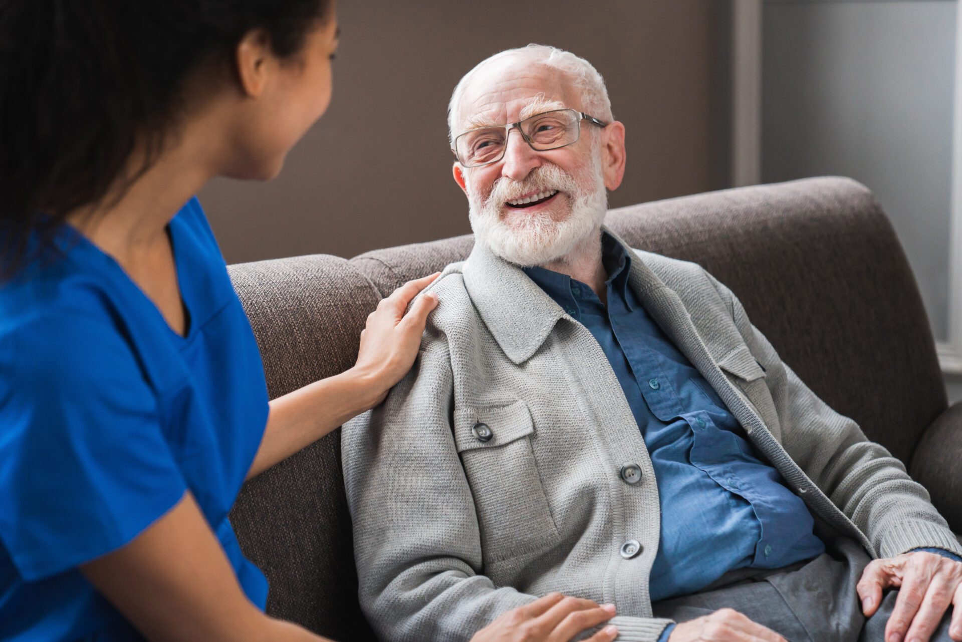 Friendly female caregiver talking chatting to happy senior man in hallway of nursing home. Picture of smiling nurse assisting senior elderly man